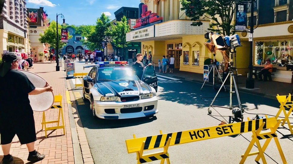 Filmset in Fußgängerzone mit Polizeiauto, Kameras und gelben Absperrungen mit "HOT SET"-Schild.
