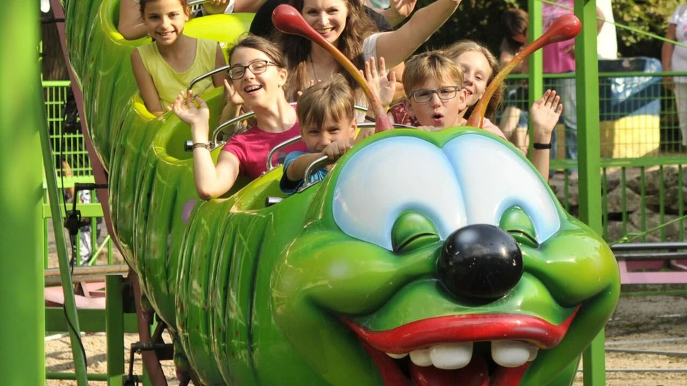 Kinder sitzen in einem Freizeitpark in einer Bahn, die wie eine Raupe gestaltet ist