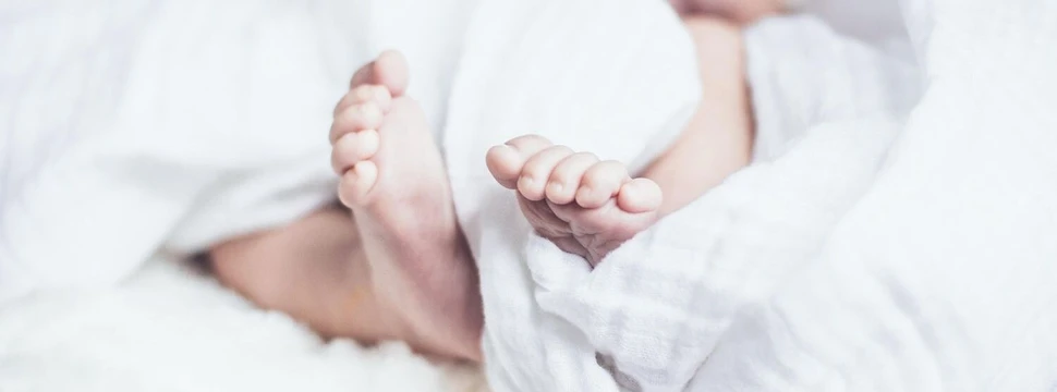 Zwei Babyfüße zwischen weißer Bettdecke