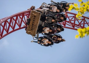 Personen in einer Achterbahn auf roten Schienen vor einem strahlend blauen Himmel