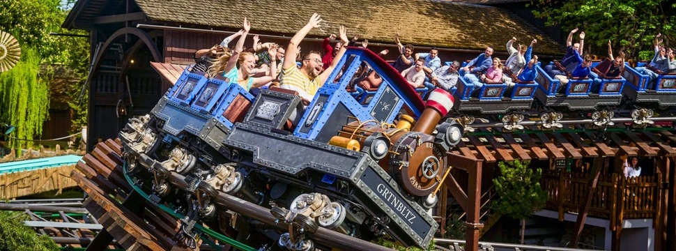 Fahrgäste mit erhobenen Armen in einer Achterbahn, die wie eine Lokomotive gestaltet ist.