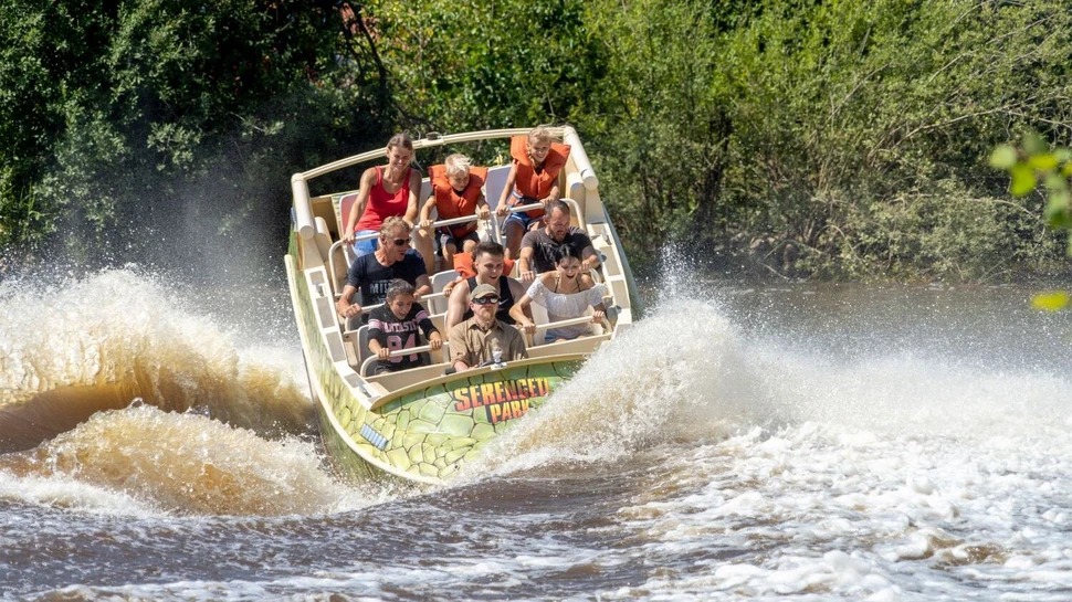 Wildwasser-Fahrgeschäft mit Besuchern in einem Boot, das ins Wasser eintaucht und hohe Wasserfontänen erzeugt.